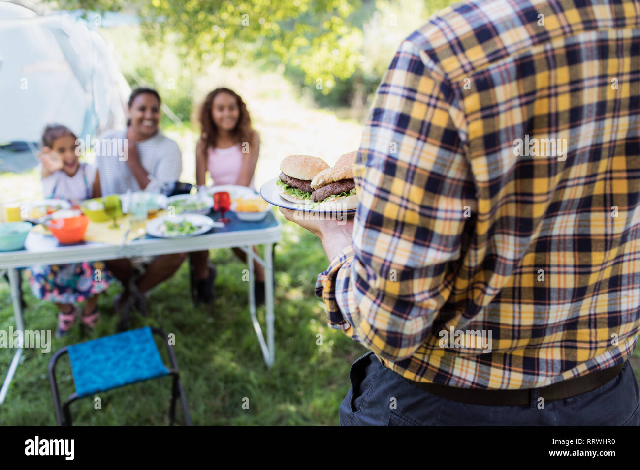 Father serving barbecue hamburgers to family at campsite table Stock Photo