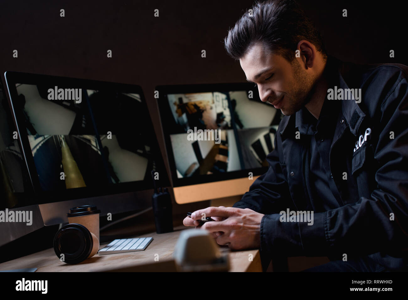 smiling guard in uniform using smartphone at workplace Stock Photo