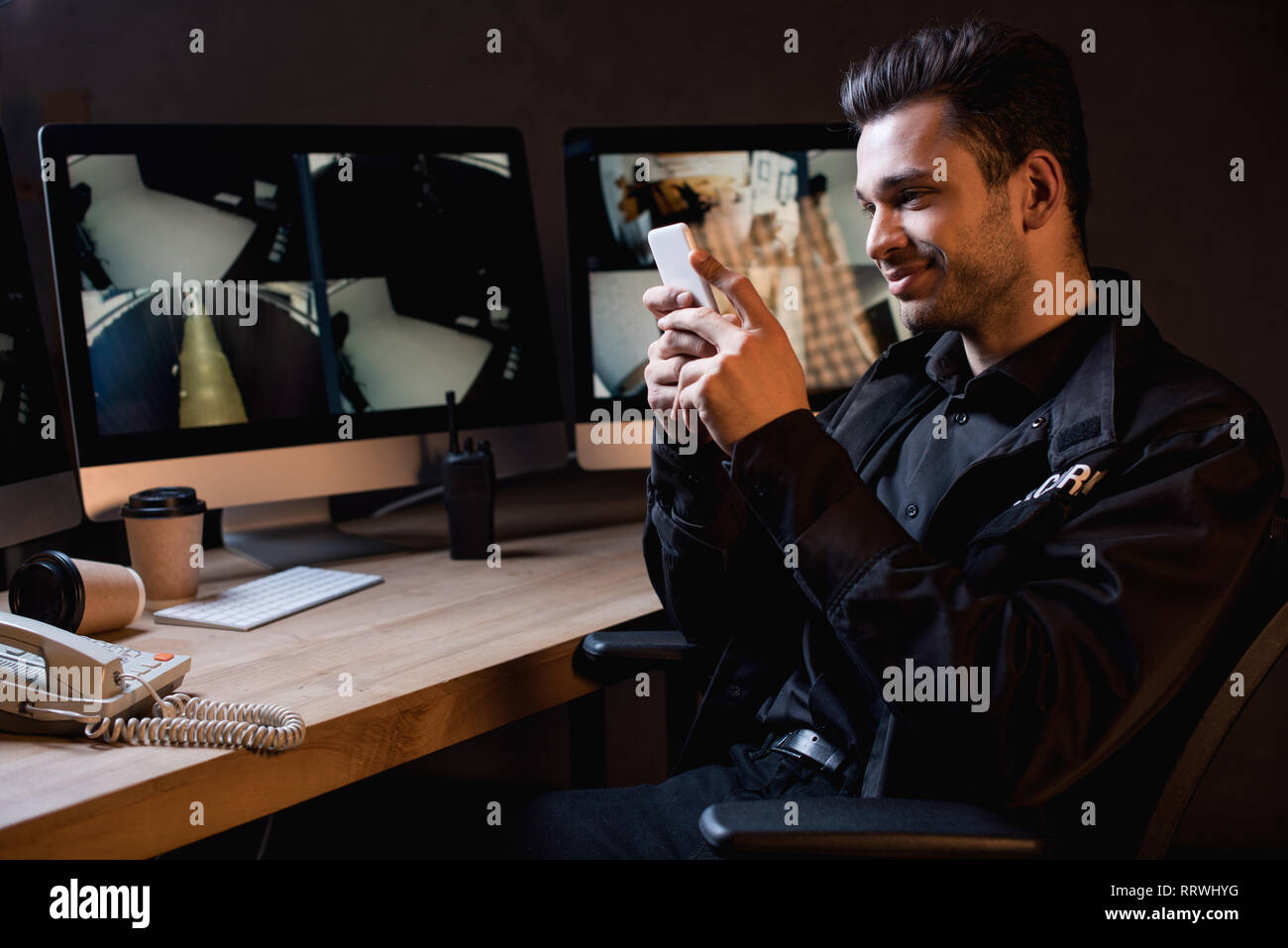 smiling guard in uniform using smartphone at workspace Stock Photo