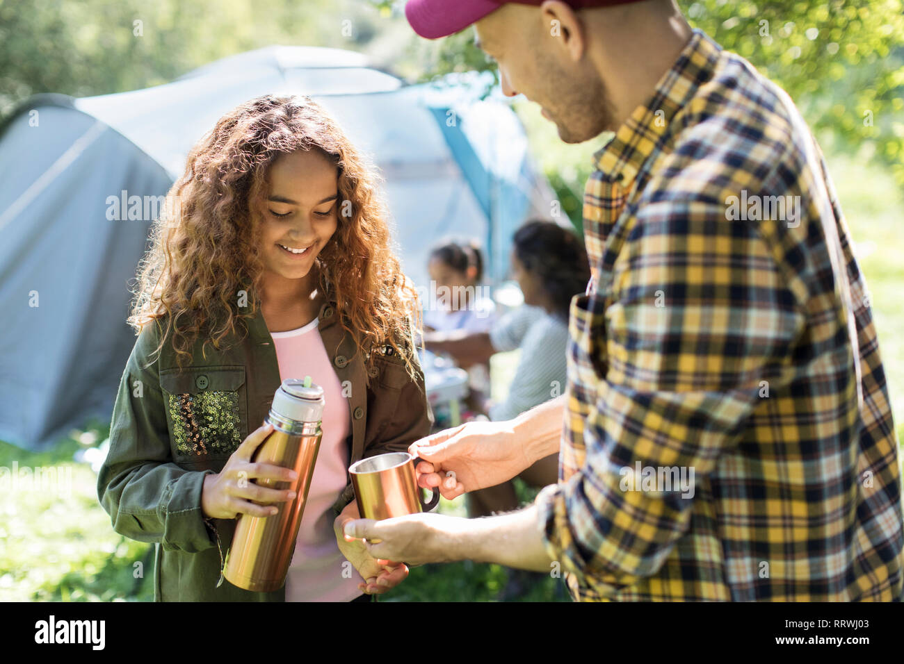 Daughter pouring coffee from insulated drink container for father at campsite Stock Photo