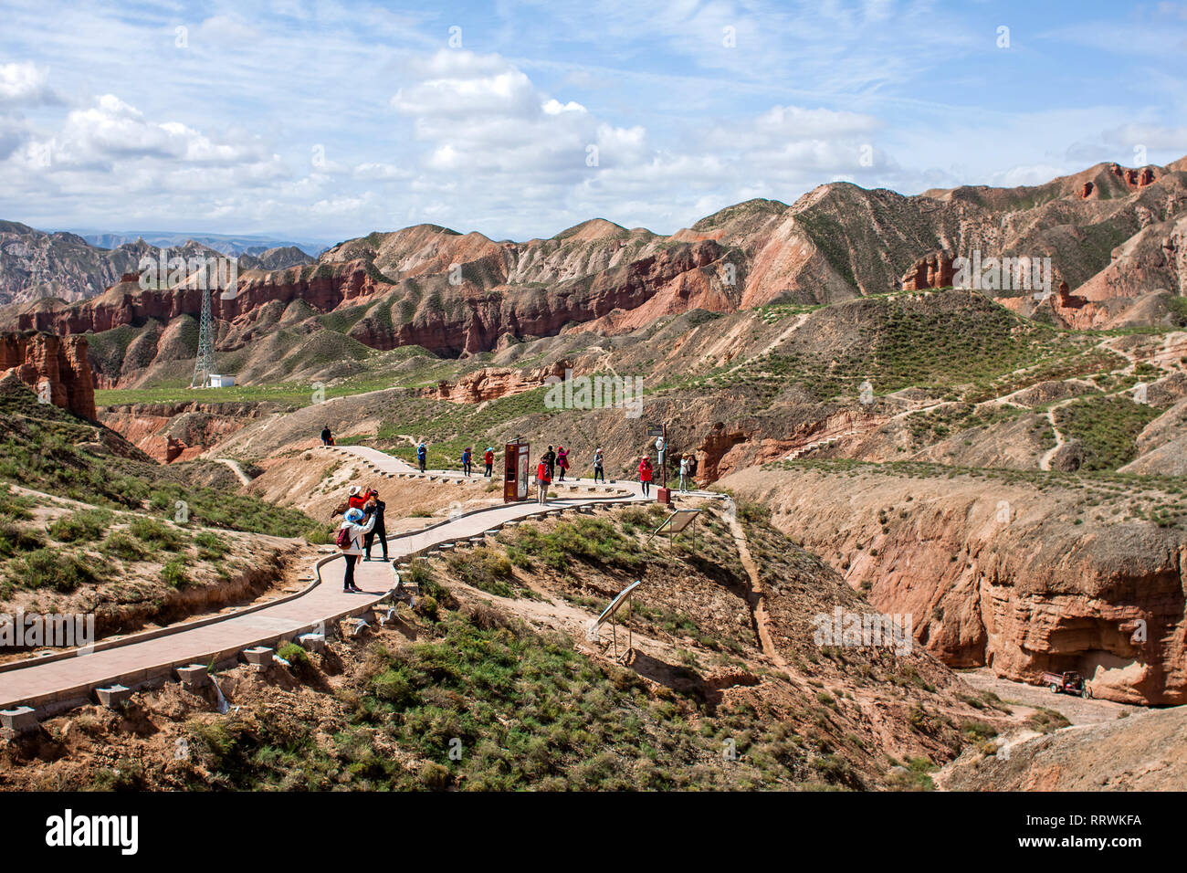 Group of Chinese Tourists are Walking Along a Path in Binggou Danxia Canyon Landform in Zhangye, Sunan Region, Gansu Province, China. Red Sandstone Stock Photo