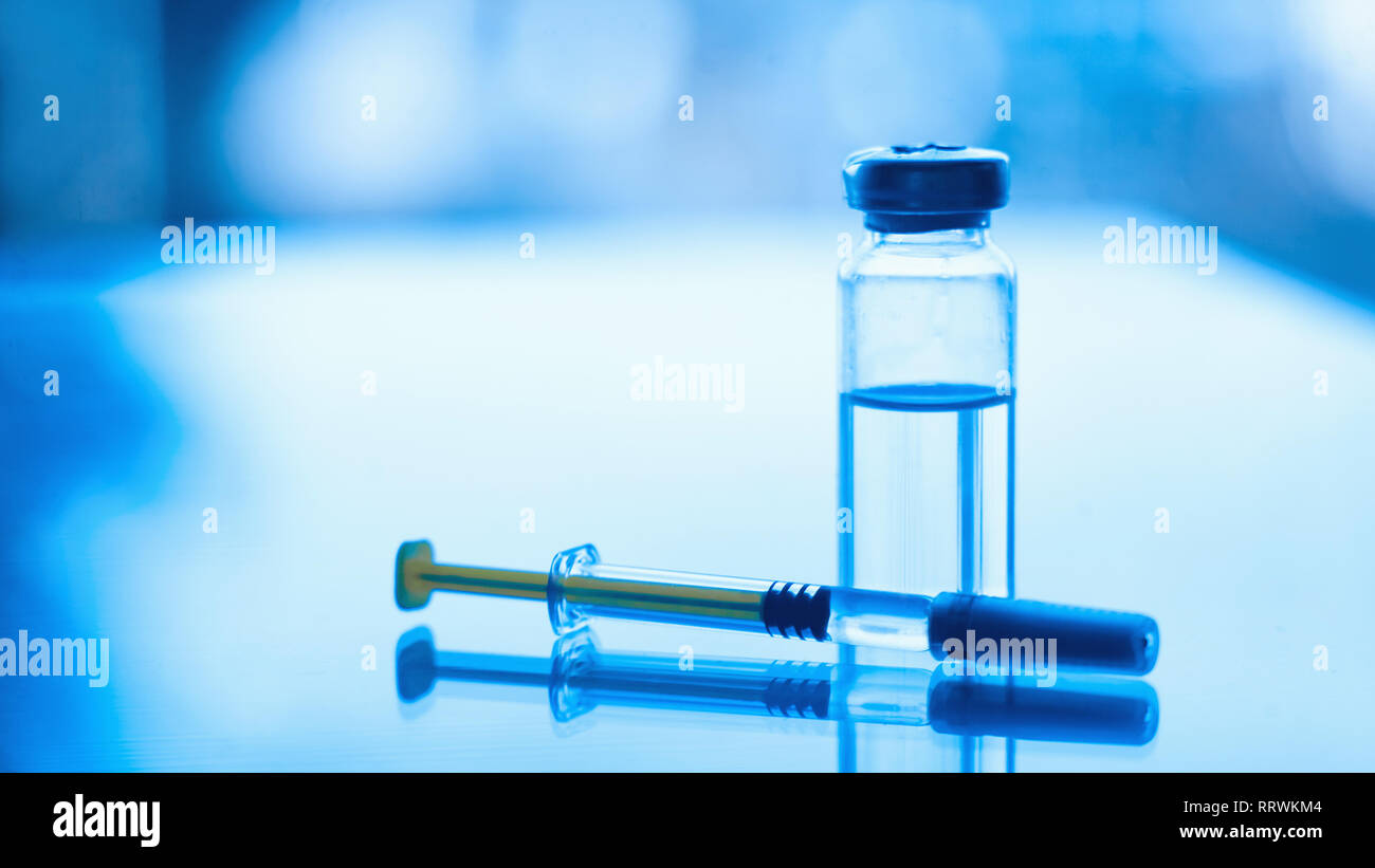 Vials of medication and syringe on a blue glass table with window ...