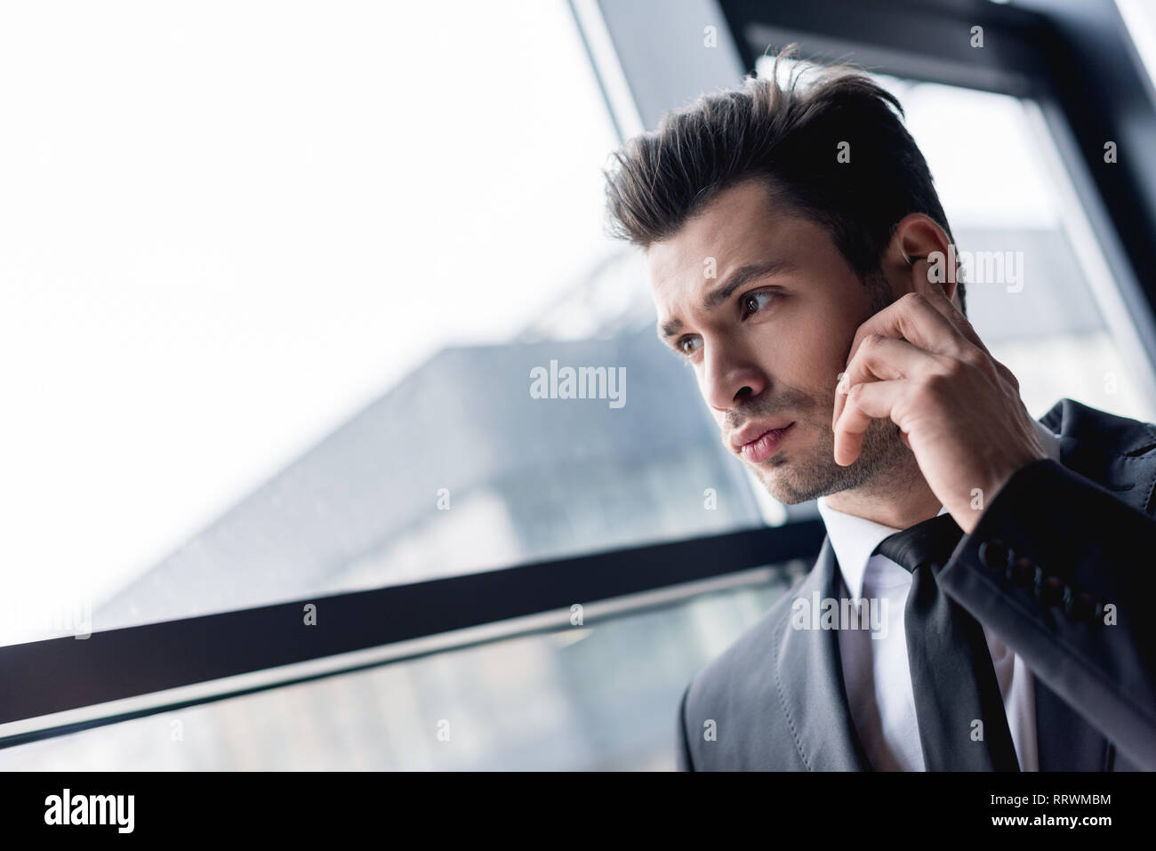 focused handsome bodyguard in suit using earphone Stock Photo