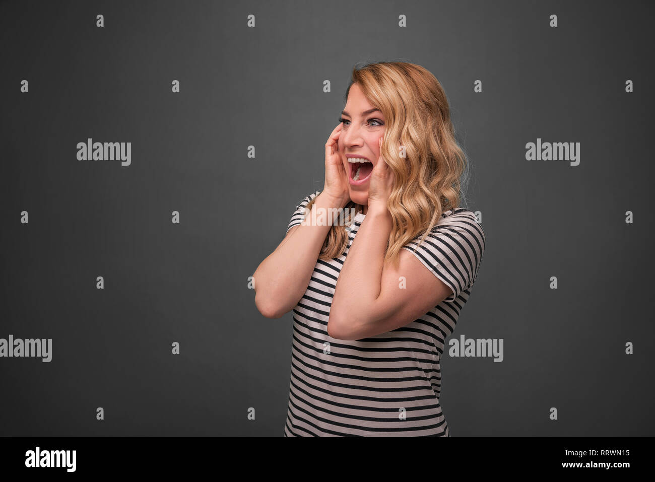 Emotional blonde screams. Frightened woman screaming straining standing on a gray background. Stock Photo