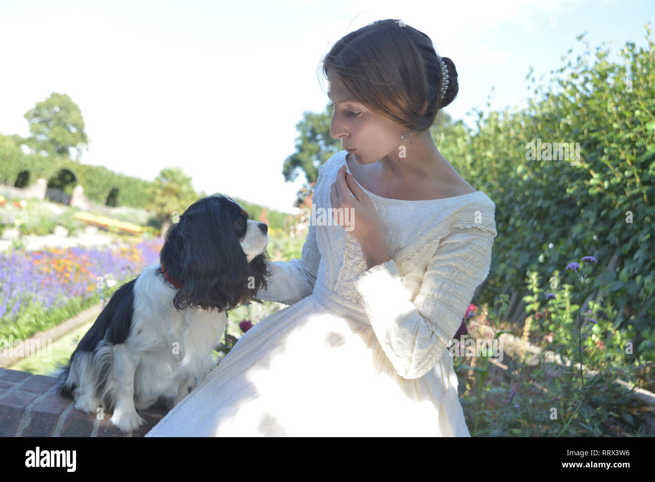 A young Queen Victoria and her dog Dash sit on a wall in the garden at