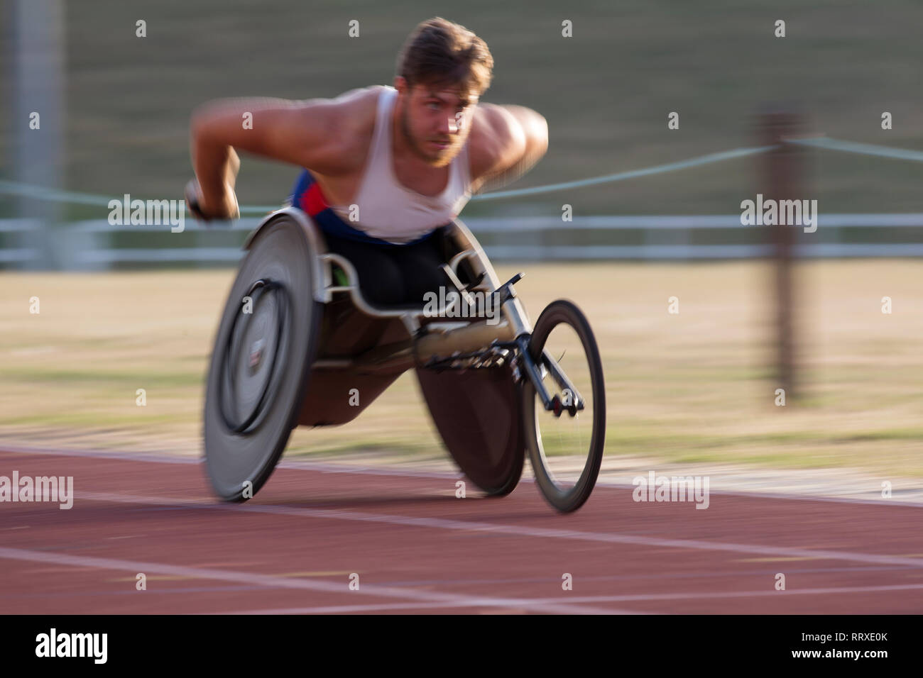 Determined young male paraplegic athlete speeding along sports track in ...