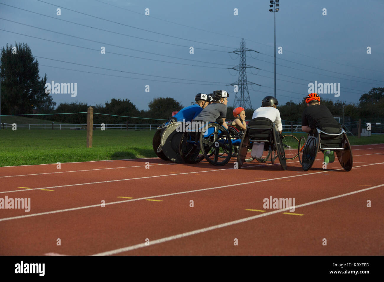 Paraplegic athletes huddling on sports track, training for wheelchair race at night Stock Photo