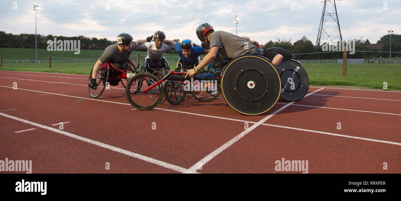 Determined paraplegic athletes bonding in huddle, training for wheelchair race on sports track Stock Photo