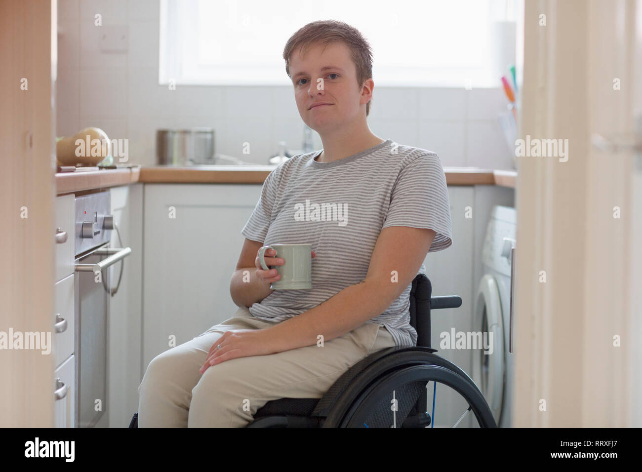 Portrait confident young woman in wheelchair drinking tea in apartment kitchen Stock Photo
