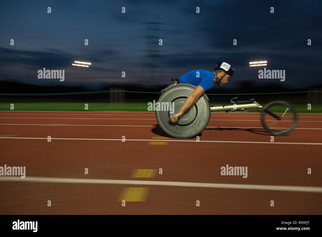 Young male paraplegic speeding along sports track during wheelchair race at night Stock Photo
