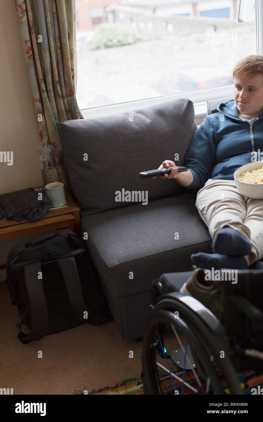 Young woman watching TV with feet up on wheelchair Stock Photo