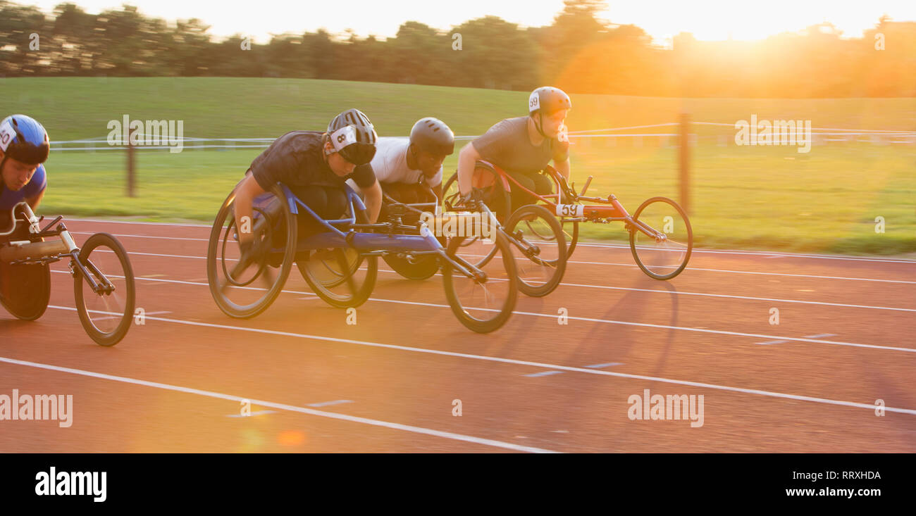 Determined paraplegic athletes speeding along sports track in wheelchair race Stock Photo