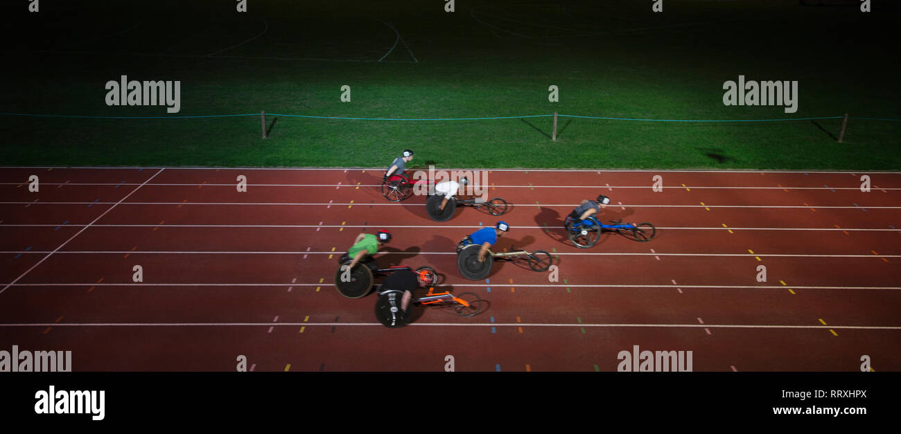 Paraplegic athletes racing along sports track in wheelchair race in night Stock Photo