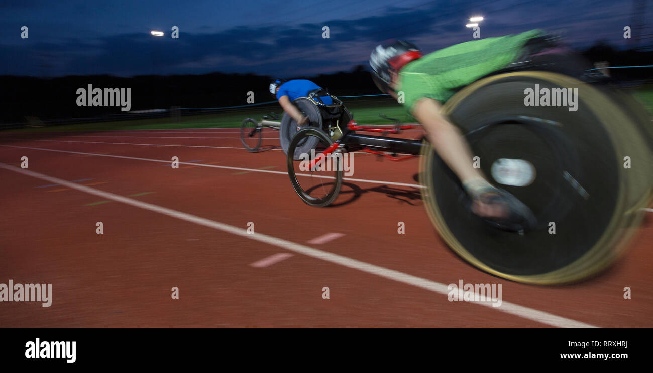 Paraplegic athletes speeding along sports track in wheelchair race at night Stock Photo