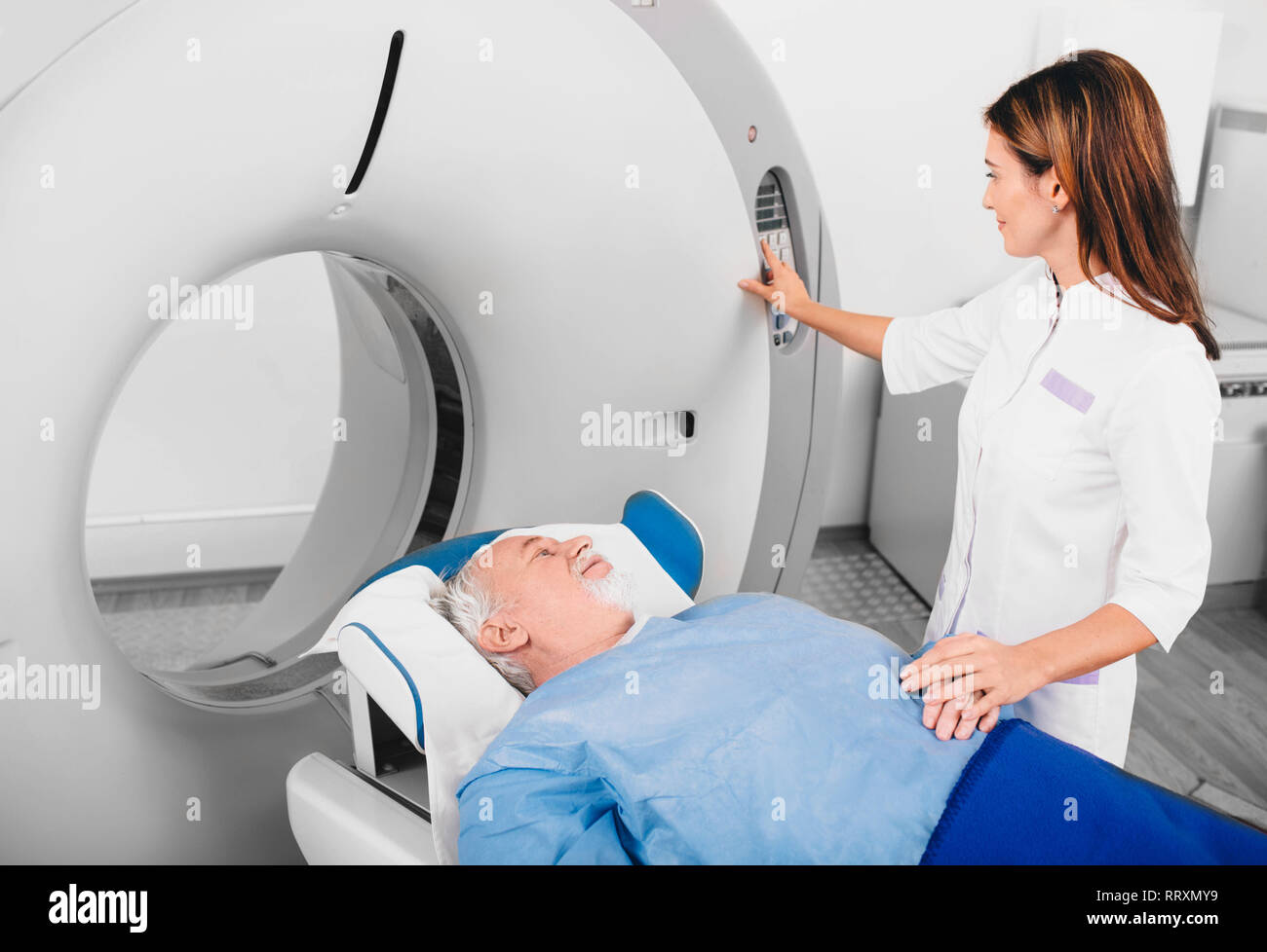 Radiographer reassuring senior man going into CT scanner in hospital Stock Photo