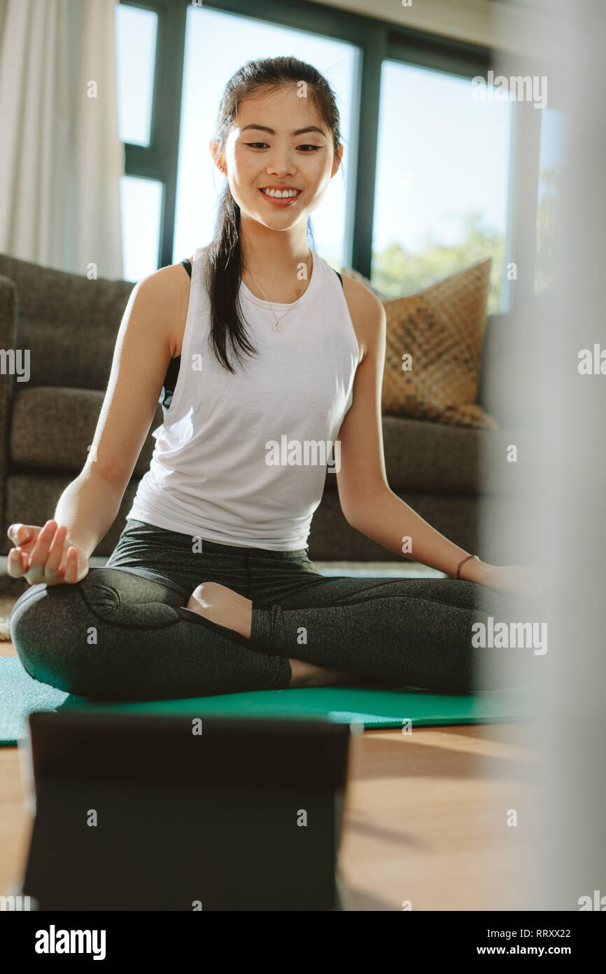 Happy young chinese woman sitting yoga pose and watching instructional  videos on digital tablet. Fit woman watching fitness tutorial on tablet  compute Stock Photo - Alamy
