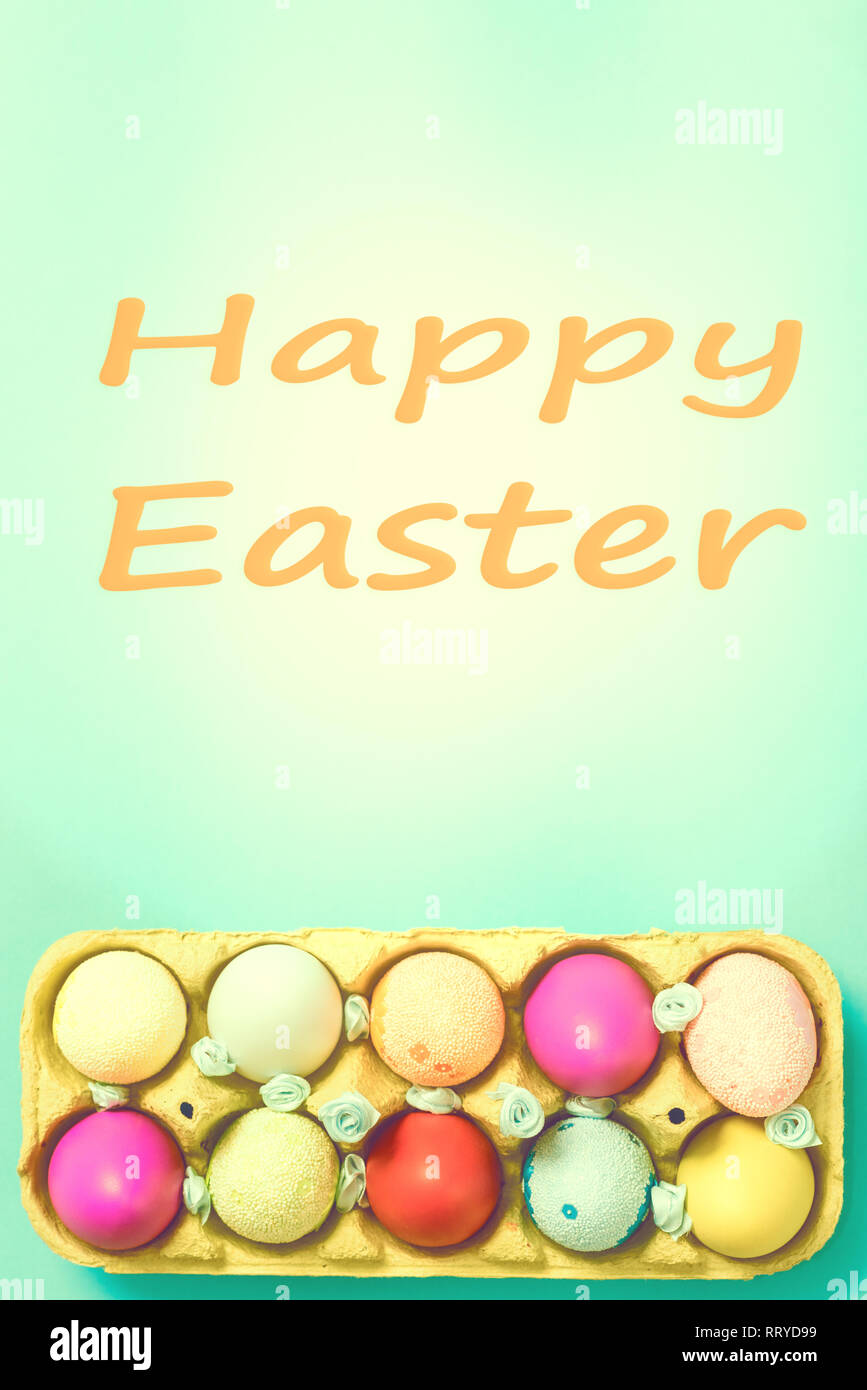 Bright Easter eggs lie in a box on a blue background. Inscription happy