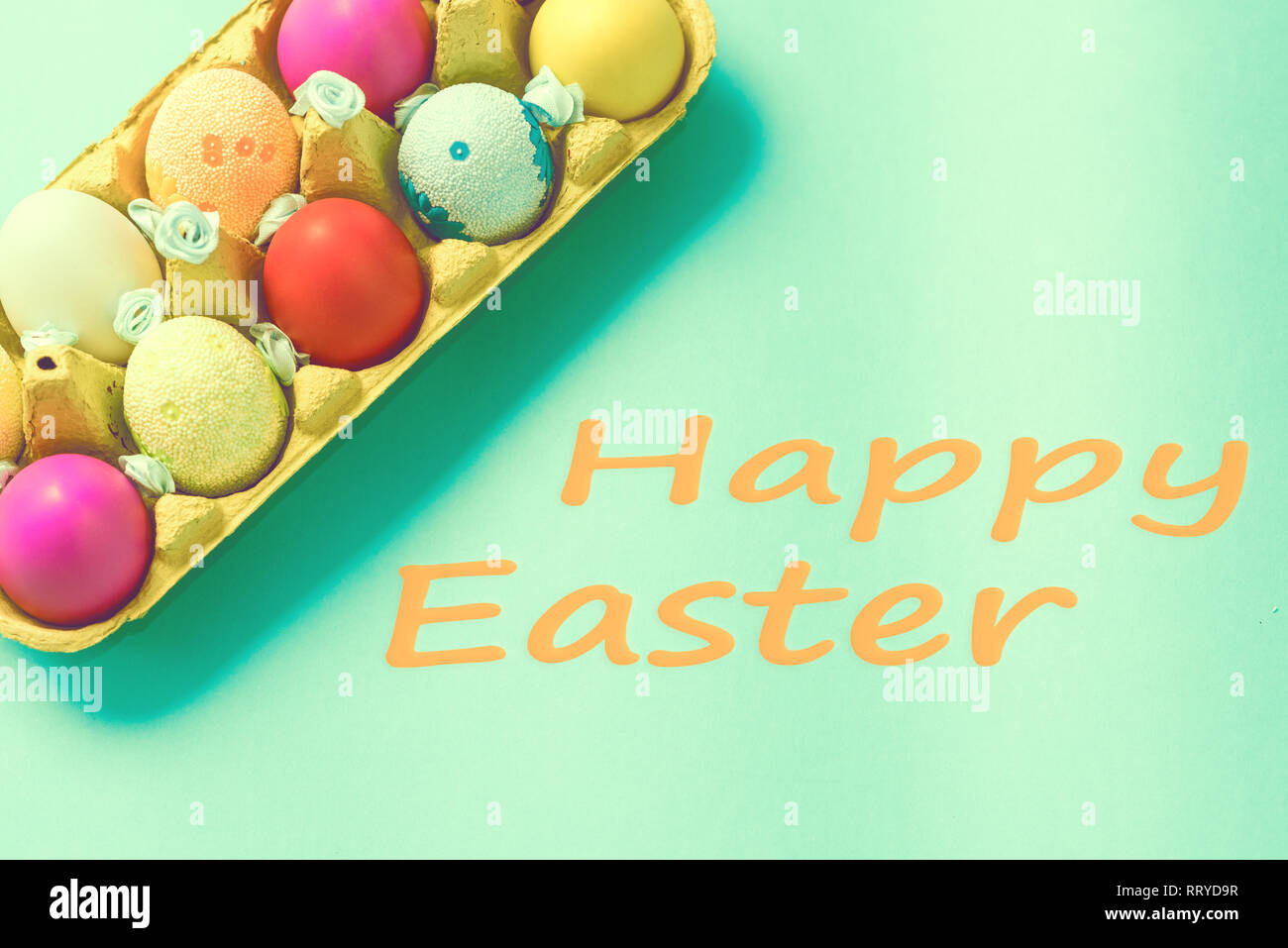 Bright Easter eggs lie in a box on a blue background. Inscription happy