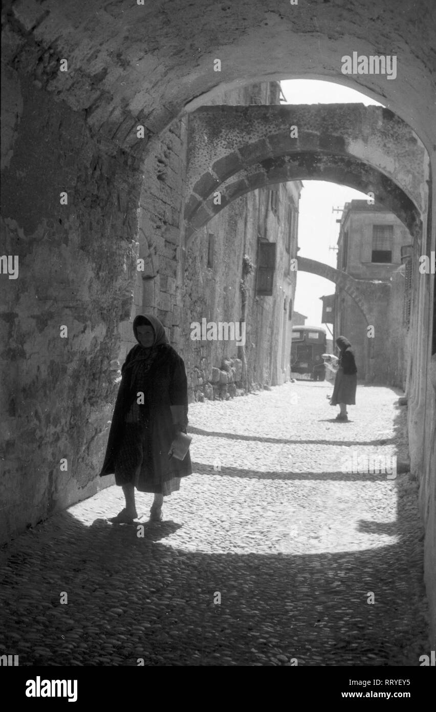 Griechenland, Greece - Frauen laufen in einer Gasse im Schatten und im Sonnenschein, Griechenland, 1950er. Women walking through a small lane in shadow and in sunshine, Greece, 1950s. Stock Photo