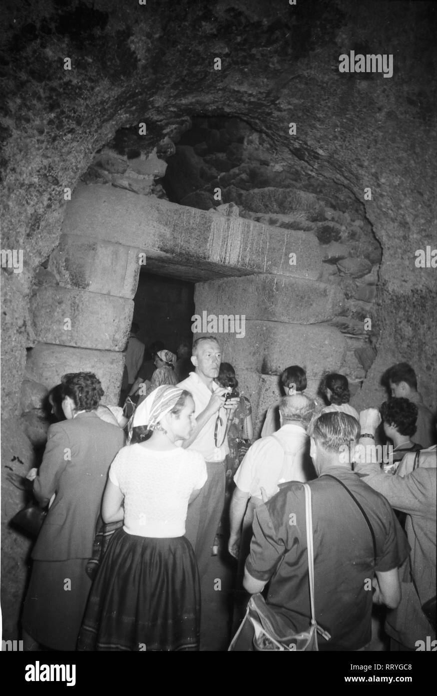 Griechenland, Greece - Eine Touristengruppe bekommt mit Kerzen als Beleuchtung ausgerüstet, das Innere des Schatzhauses des Atreus erläutert, Griechenland 1950er Jahre. A group of tourists with candles going inside the treasury of Atreus in Greece, 1950s. Stock Photo