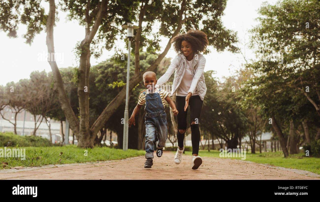 Young mother running with little boy in the park. Happy woman and cute kid having fun outdoors. Stock Photo
