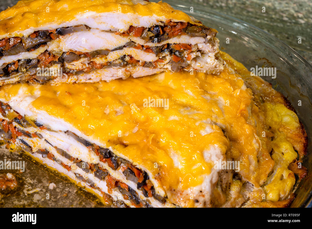 Baked in a glass baking tray in the oven, a layered meat pie with mushrooms and vegetables, covered with melted cheese, ready to eat, cut into pieces  Stock Photo