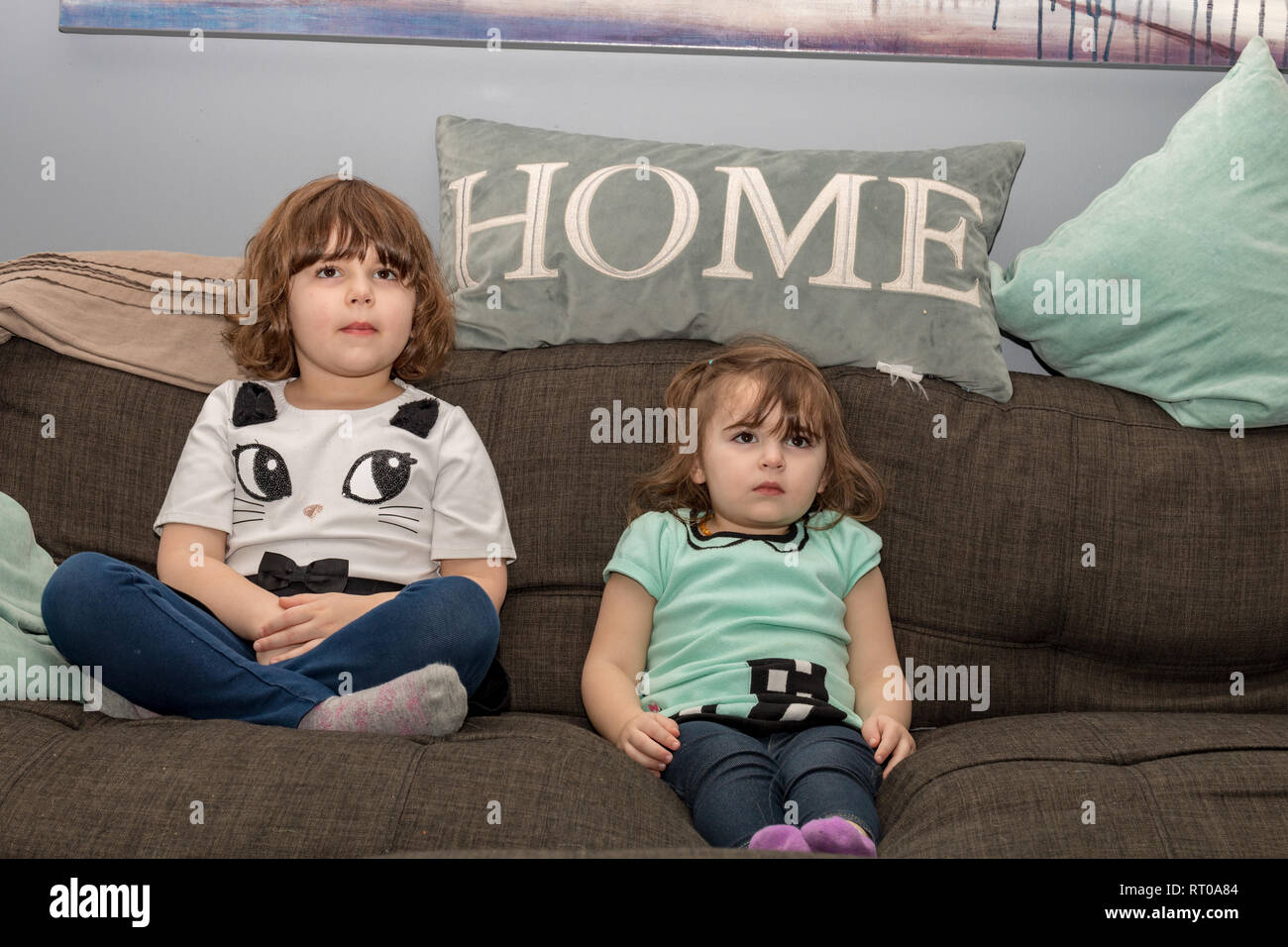Two sisters at home watching TV on the couch. Stock Photo