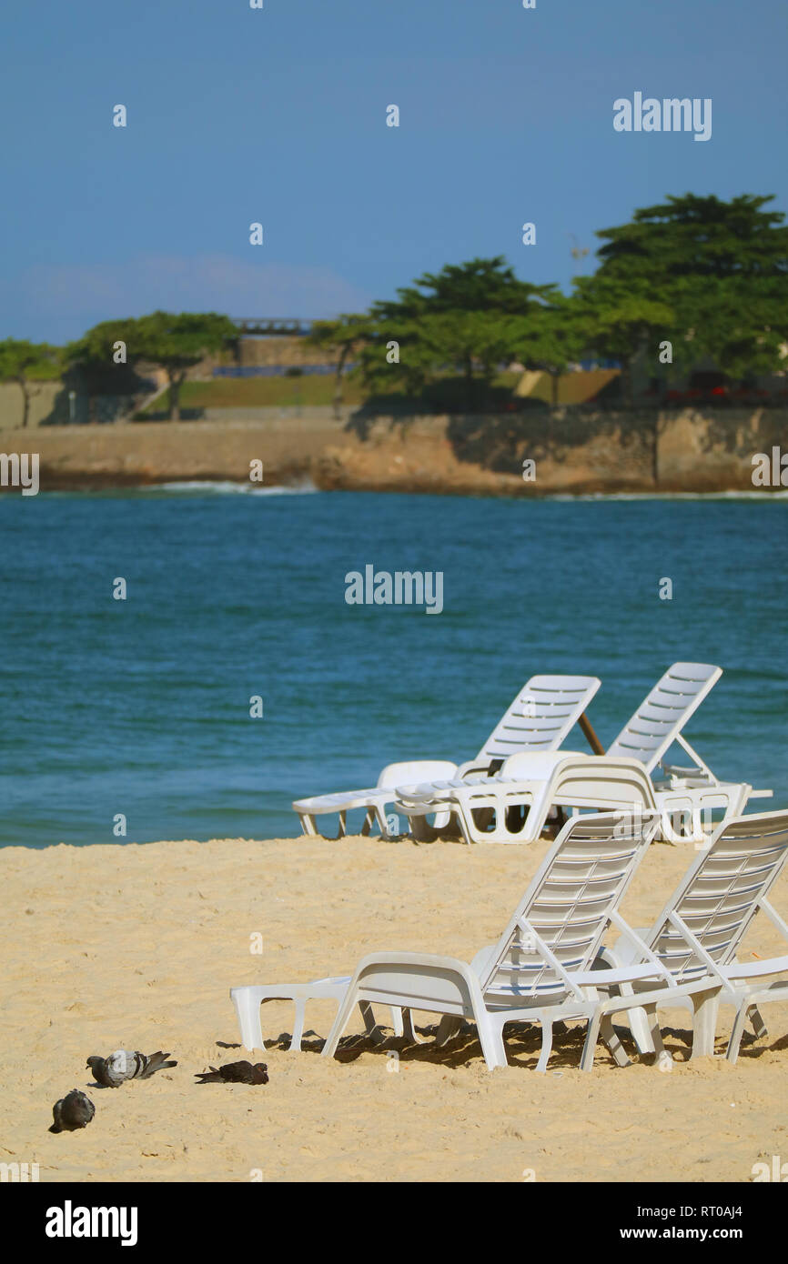 White beach chairs with group of Pigeons sunbathing on the sandy beach of Copacabana, Rio de Janeiro, Brazil, South America Stock Photo