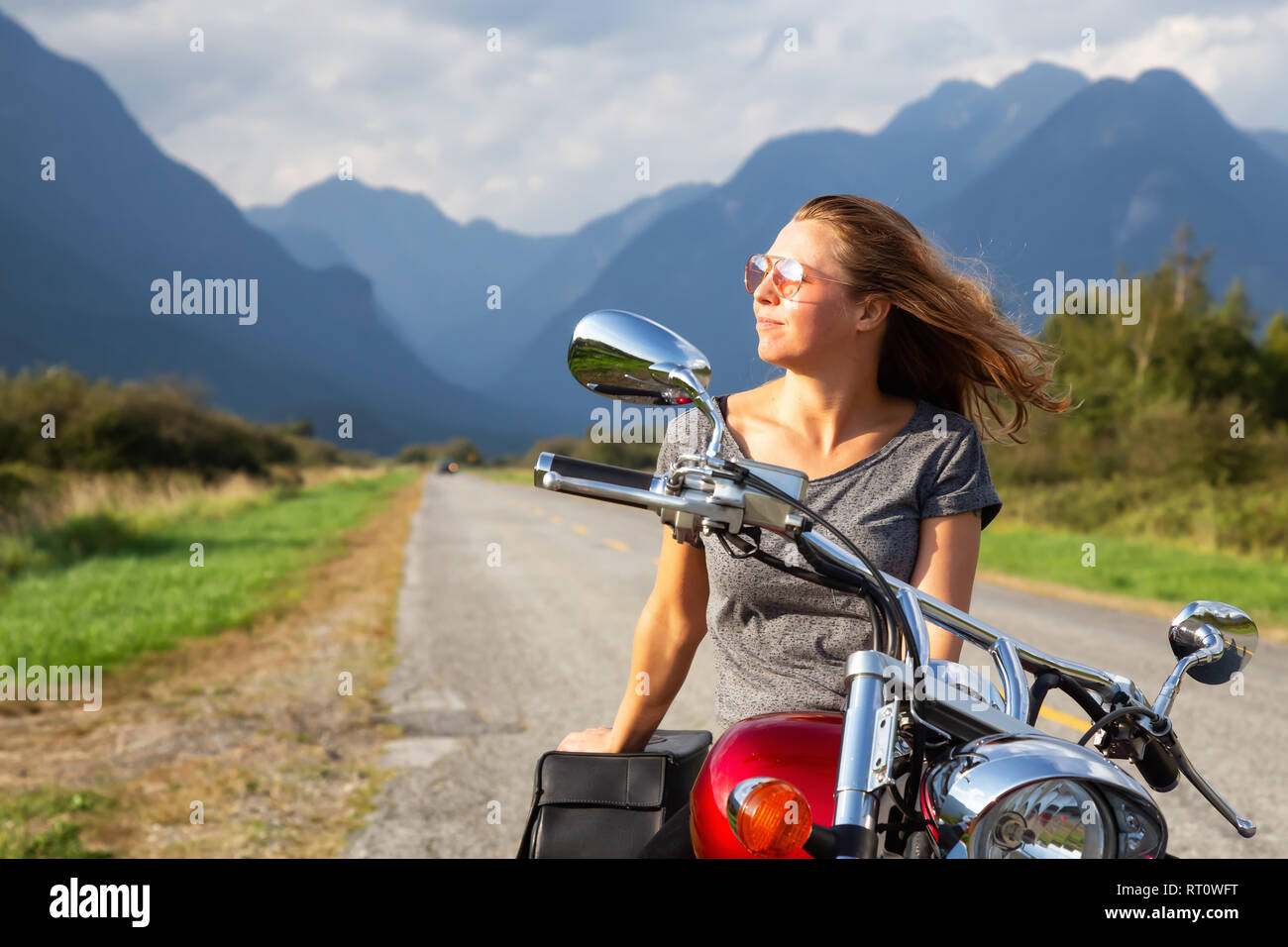 Woman riding a motorcycle on a scenic road surrounded by Canadian Mountains. Taken in Pitt Meadows, Greater Vancouver, BC, Canada. Stock Photo