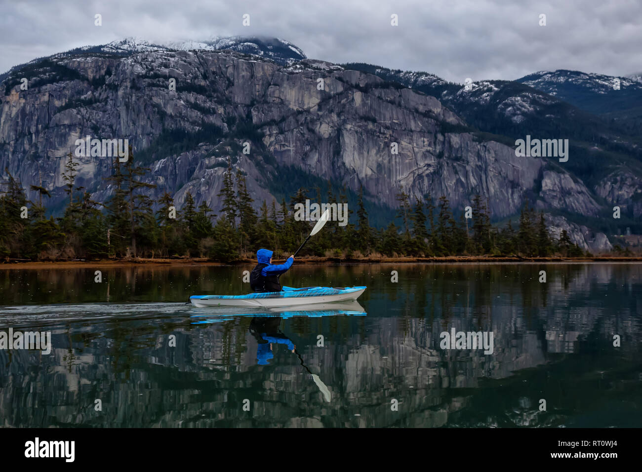 Adventurous man kayaking in peaceful water during a cloudy winter sunset. Taken in Squamish