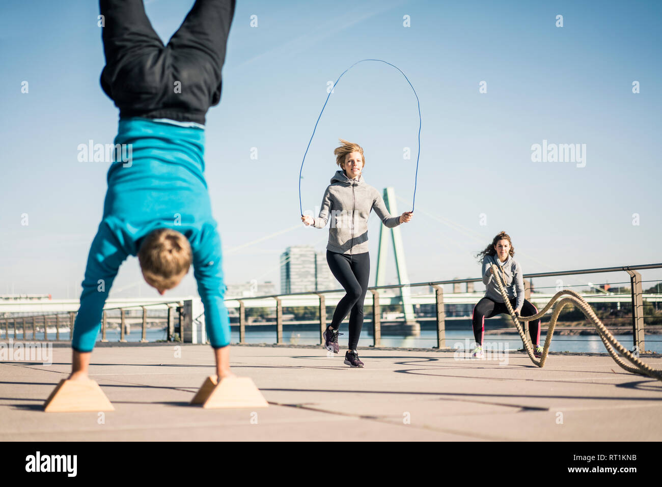 Friends training at the riverside, skipping rope and doing handstand Stock Photo