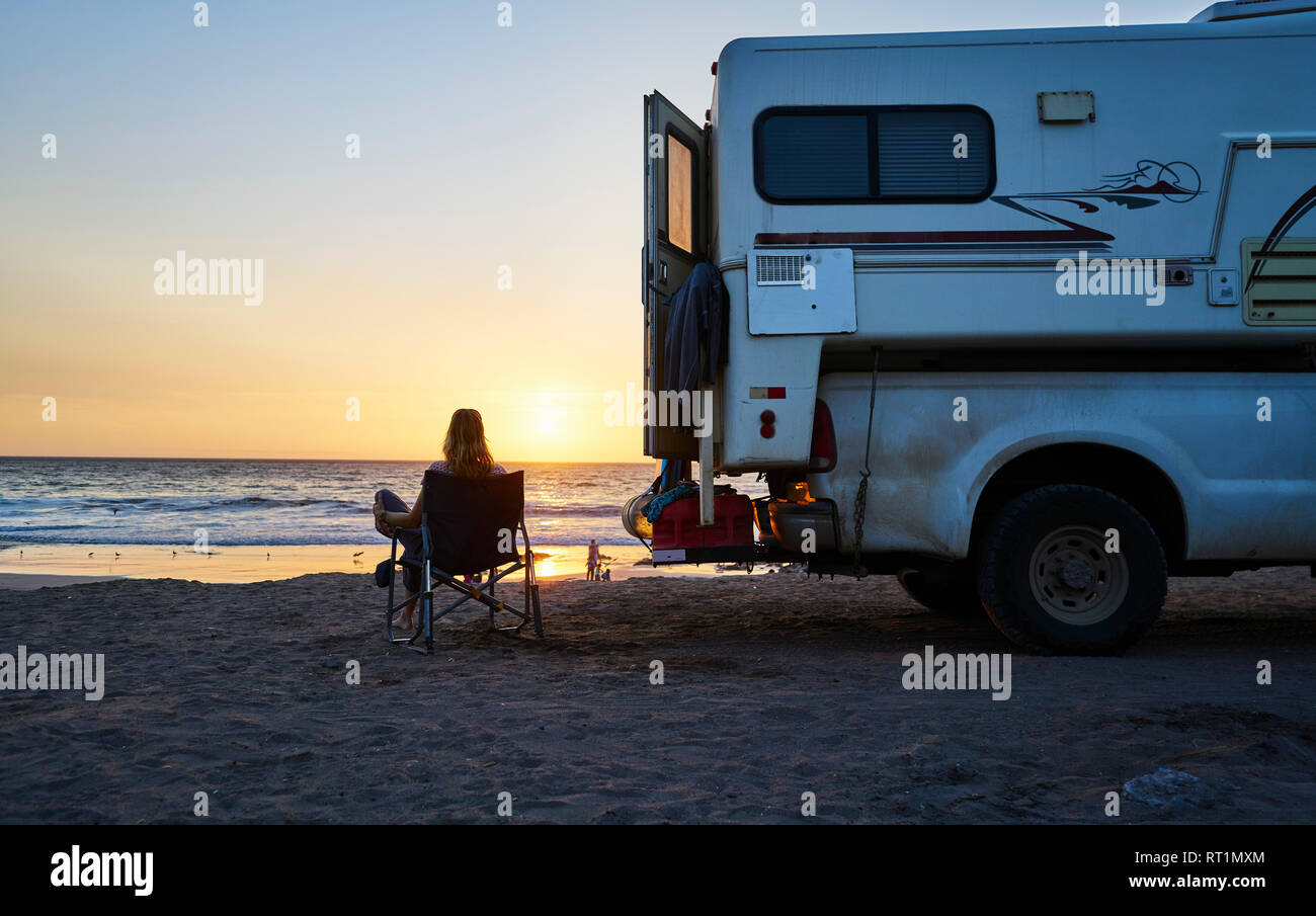 Chile, Arica, woman sitting next to camper on the beach at sunset Stock Photo