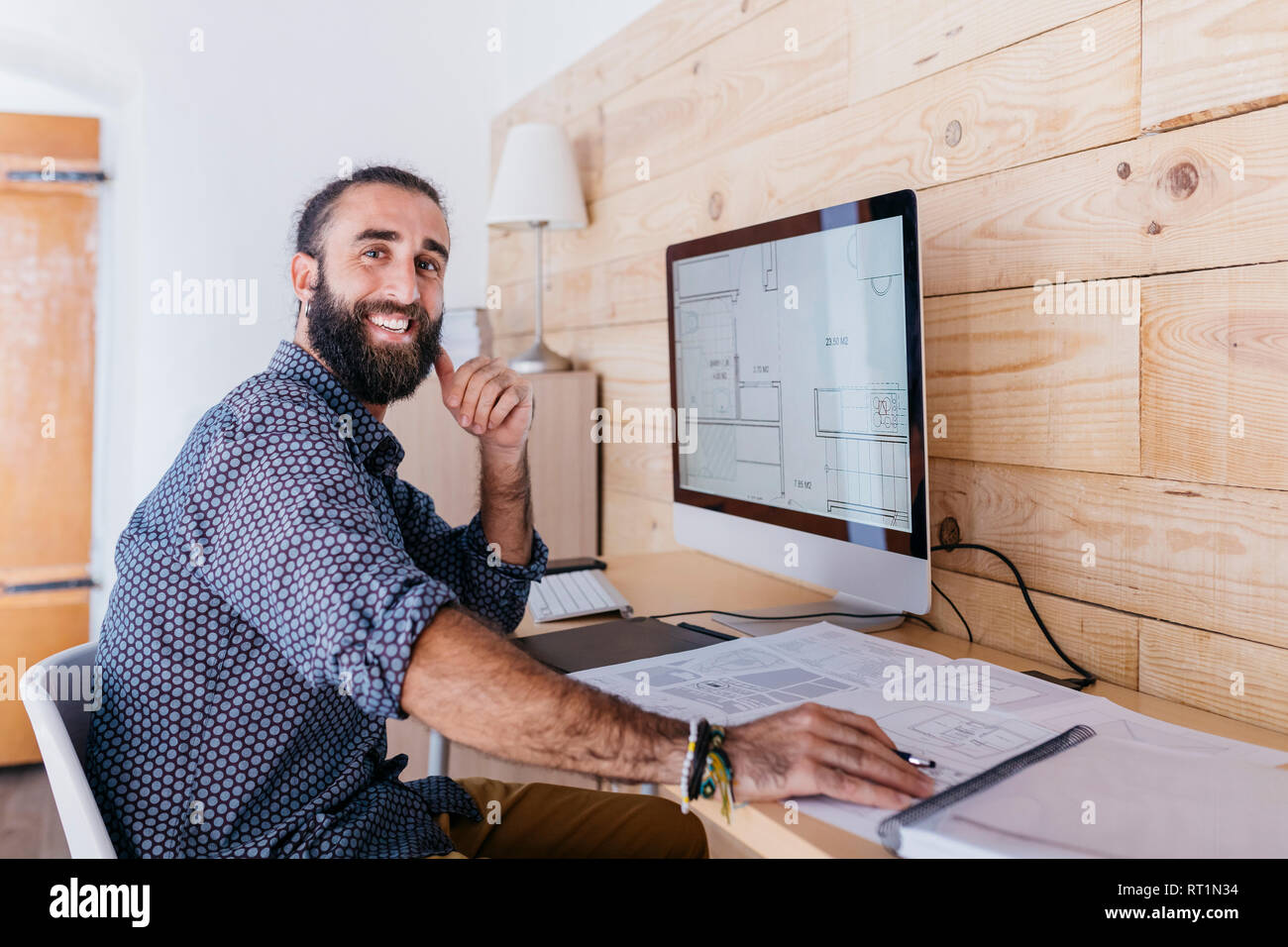 Portrait of happy young architect working at home with blueprints and computer Stock Photo
