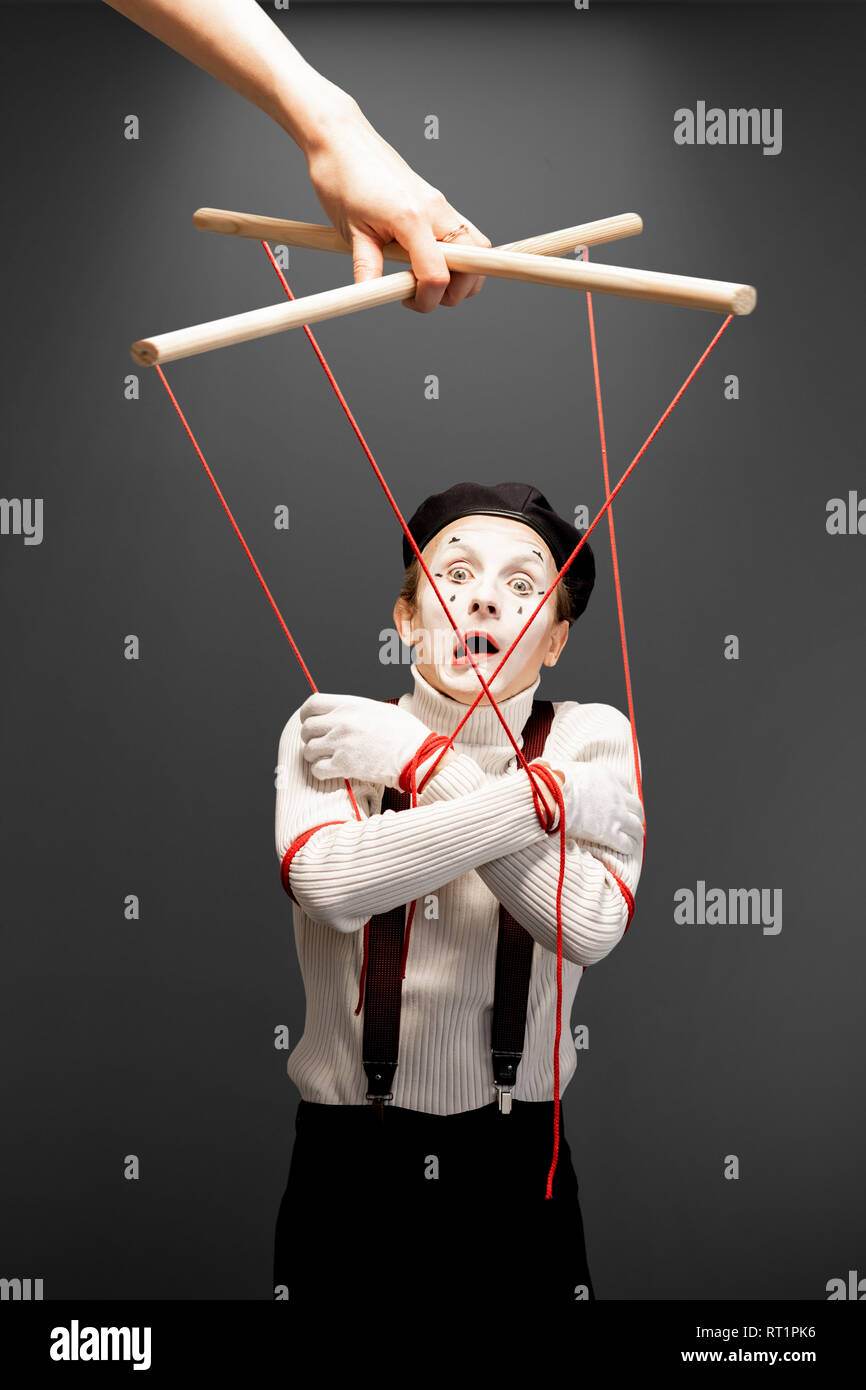 Actor as a marionette controlled with ropes by a huge hand on the grey background. Concept of a human controlling Stock Photo
