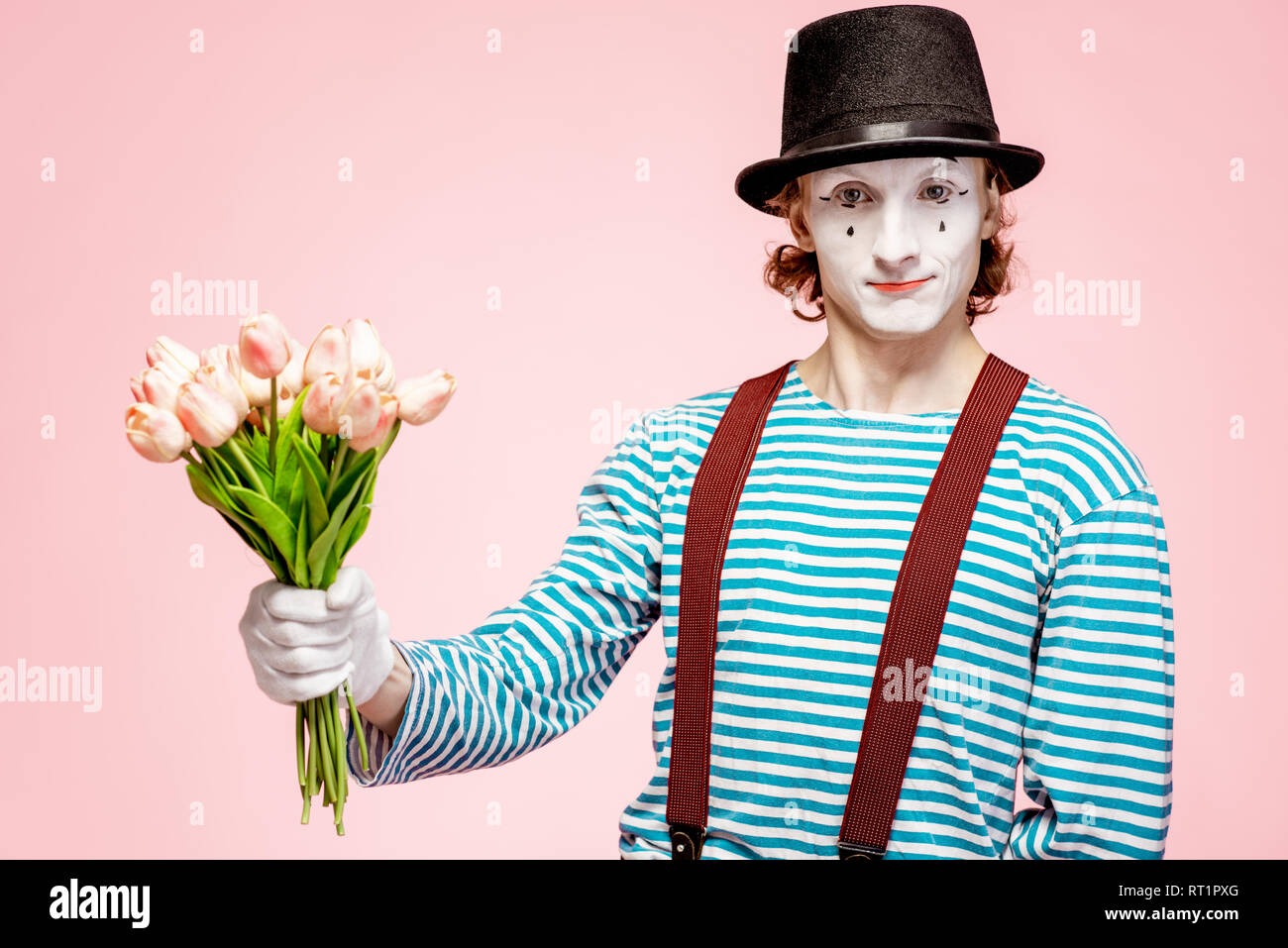 Emotional pantomime posing with tulip bouquet on the pink background indoors. Valentine's Day and love concept Stock Photo