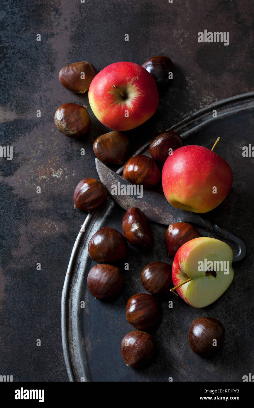 Sliced and whole apples, sweet chestnuts and an old knife on rusty background Stock Photo