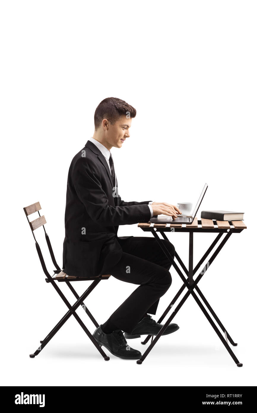 Full length profile shot of a young man in a suit sitting at a coffee table and working on a laptop isolated on white background Stock Photo