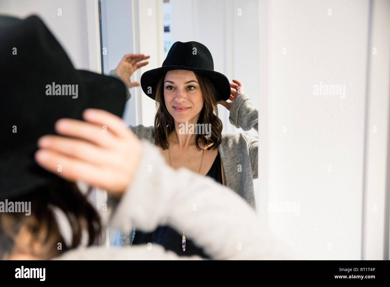 Mature woman standing in front of mirror , putting on a hat Stock Photo