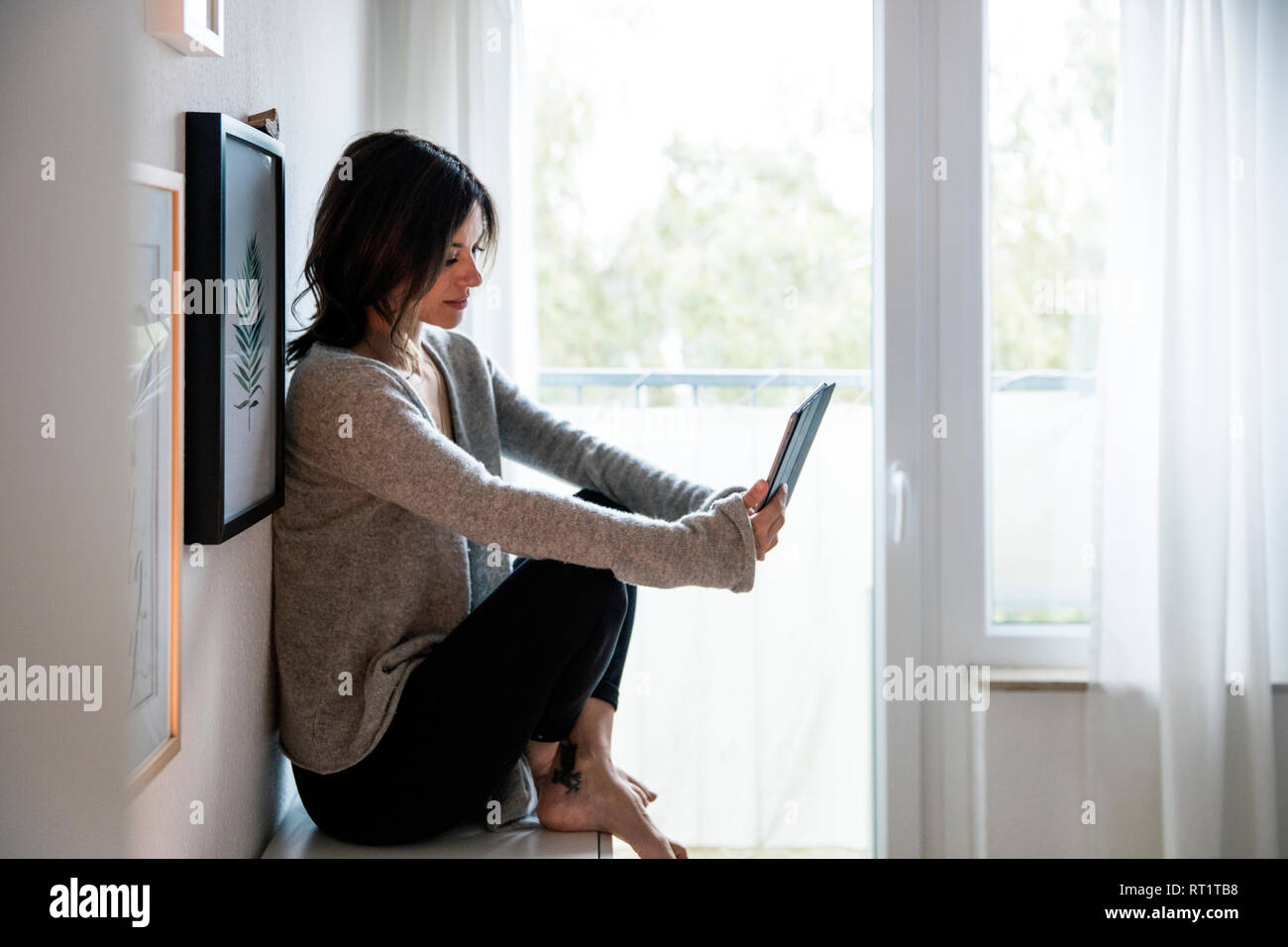 Woman sitting on chest of drawers, reding e-book Stock Photo