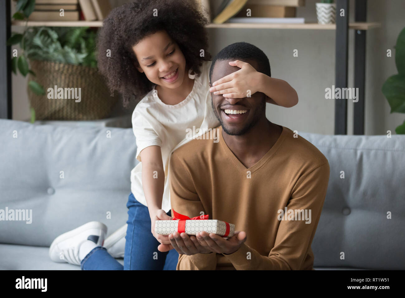 African kid daughter closing eyes congratulating dad giving gift box  Stock Photo