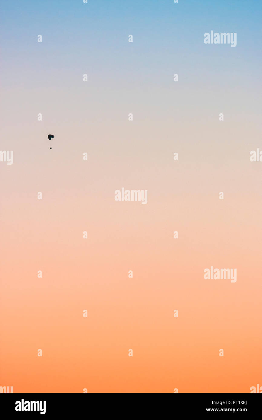 Small figure doing sky diving during sunset with a gradient background Stock Photo