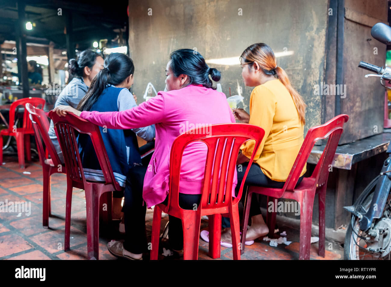 Four friends enjoy noodle and rice dishes in a busy indoor market food stall in Cambodia, Phnom Penh. Stock Photo