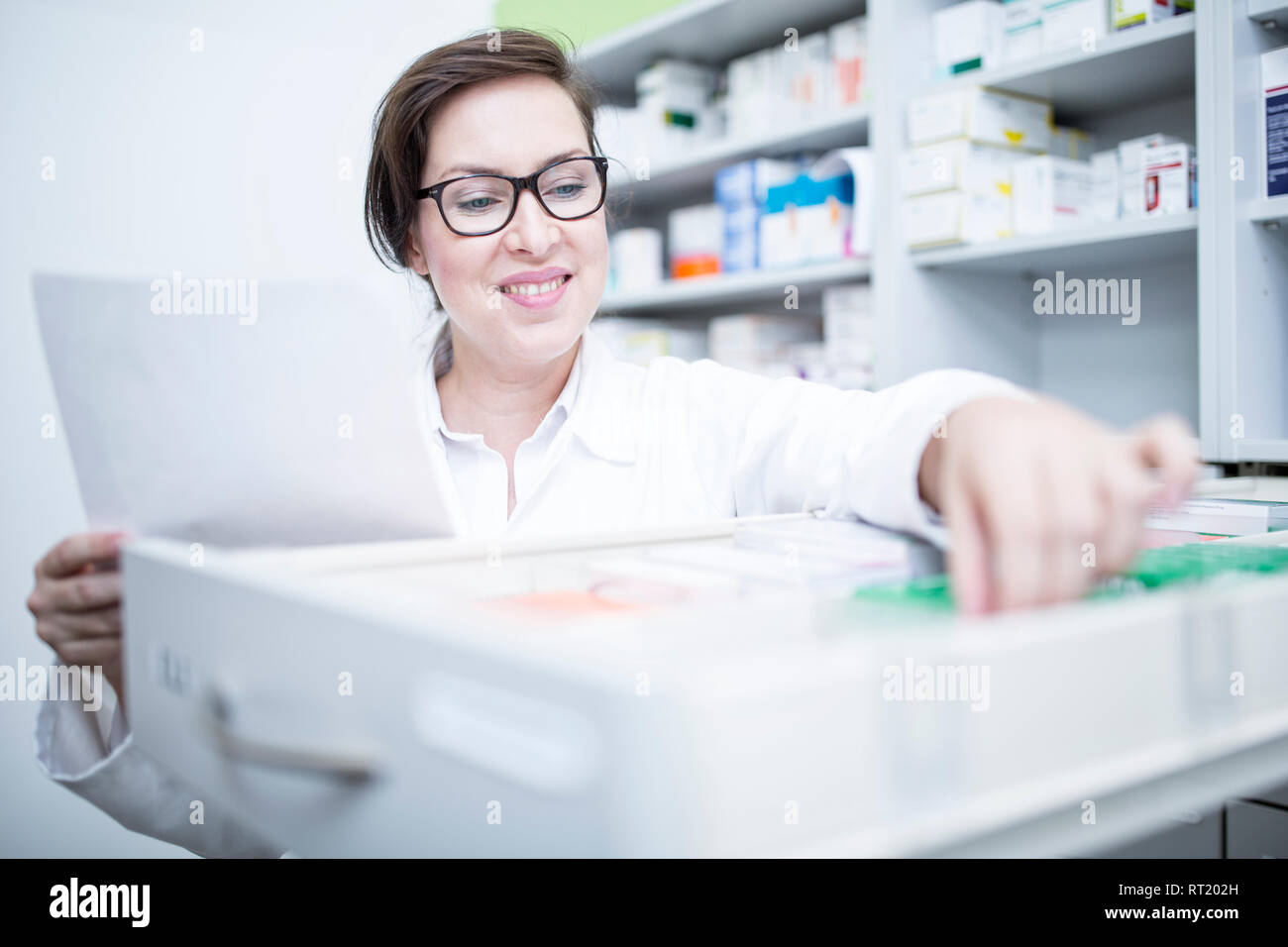 Smiling pharmacist seeking out medicine at cabinet in pharmacy Stock Photo