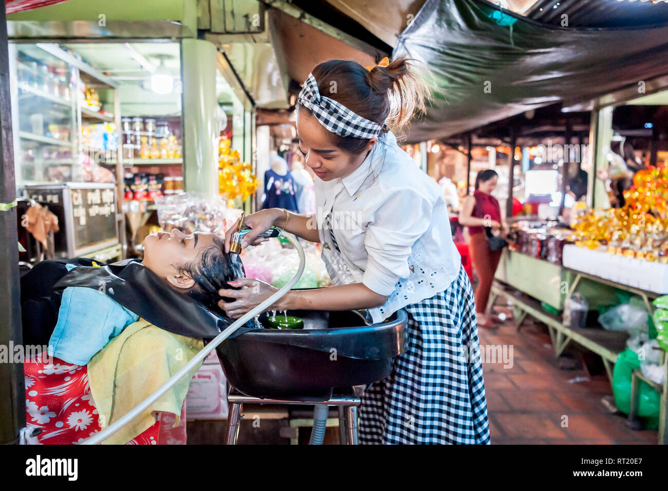 A lady washes and cuts ladies hair in a hair salon in a busy indoor market in Phnom Penh, Cambodia. Stock Photo