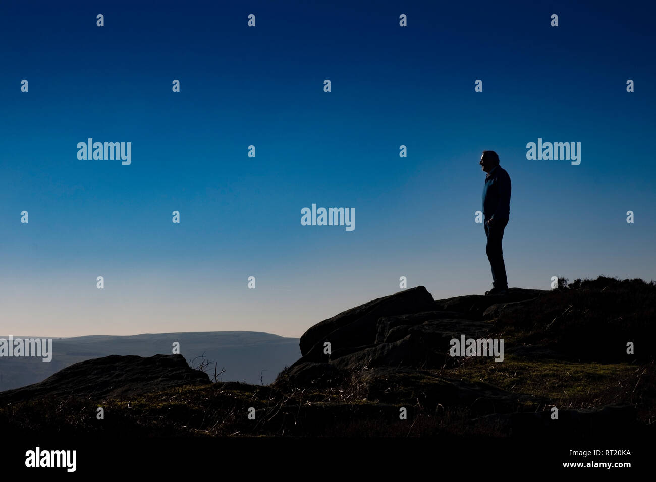 Senior man standing on cliff edge, 60s age group, silhouette against clear sky Stock Photo