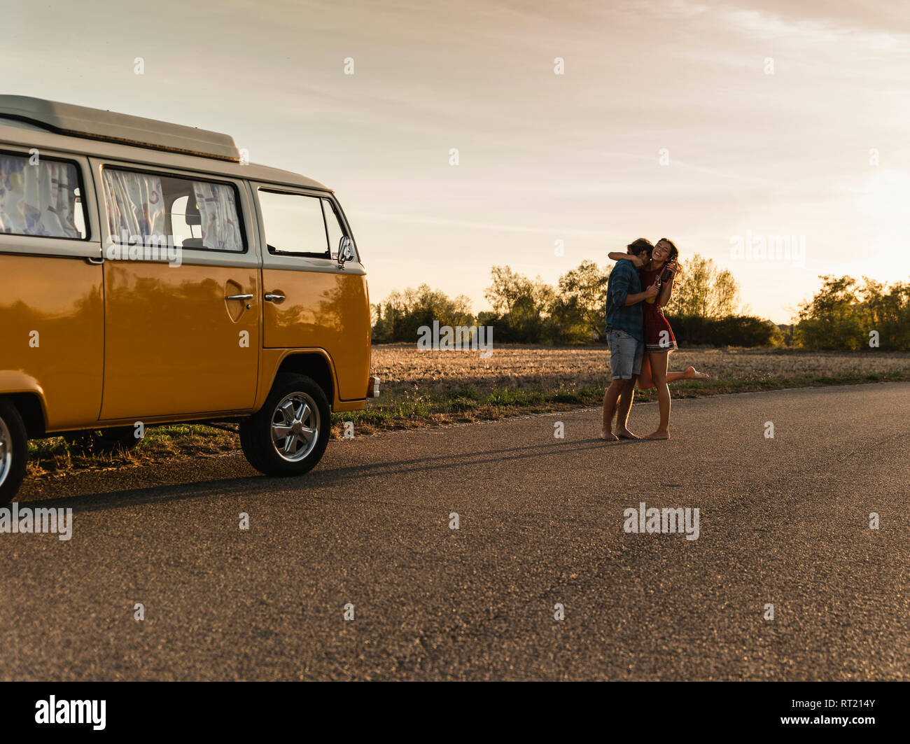 Happy couple doing a road trip with a camper, laughing and embracing on the road Stock Photo