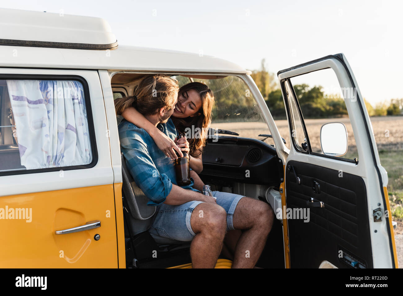 Happy couple sitting in their camper, embracing, drinking beverage Stock Photo