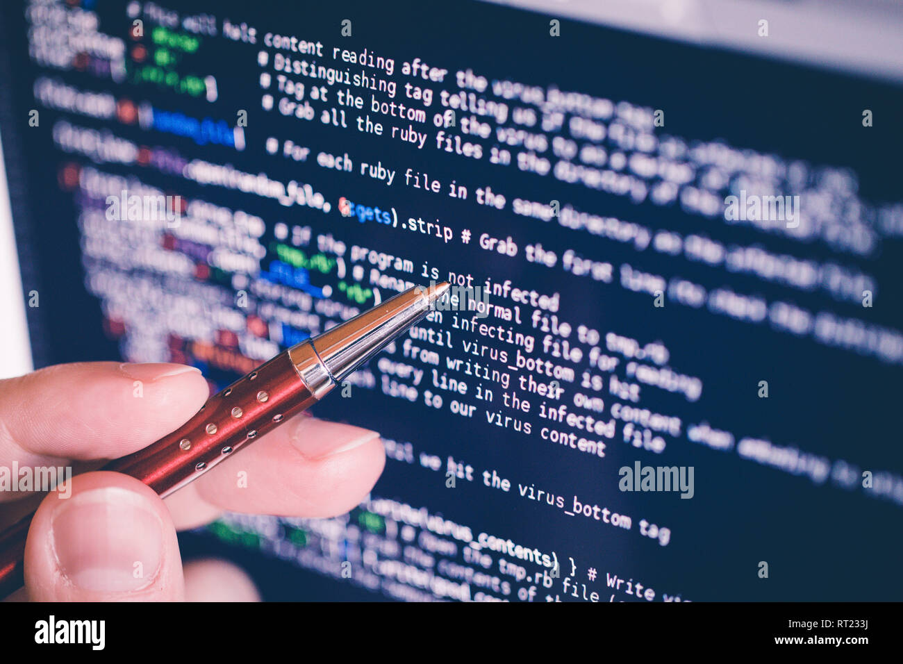 pointing on software code at the computer screen with pen, closeup