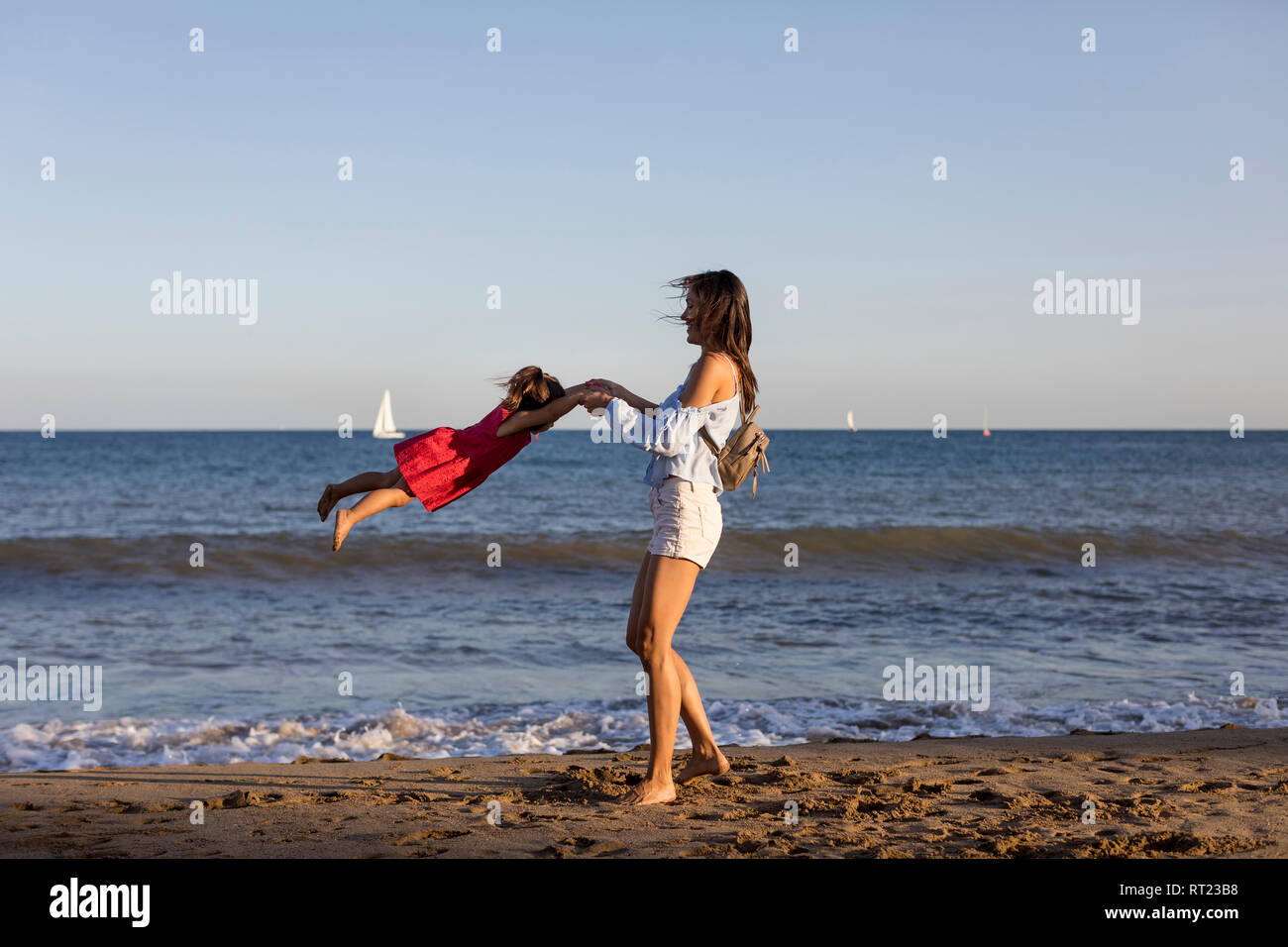 Mother and daughter having fun on the beach, pretending to fly Stock Photo