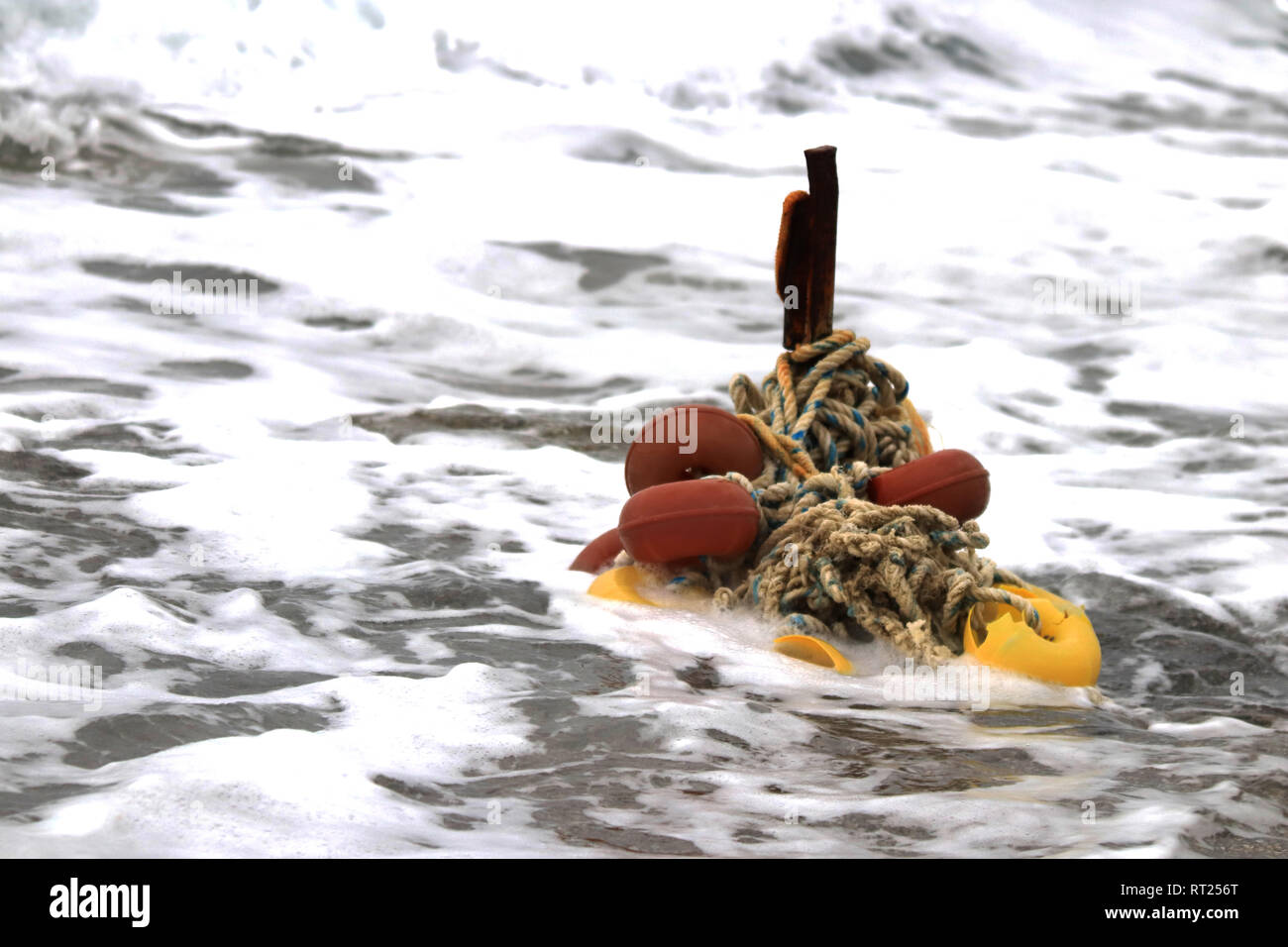 Iron stake with wound ropes and buoys in the breaking wave Stock Photo